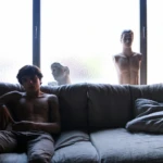 Shirtless man on sofa with male mannequins behind him, symbolising gay straight men fantasies and identity confusion